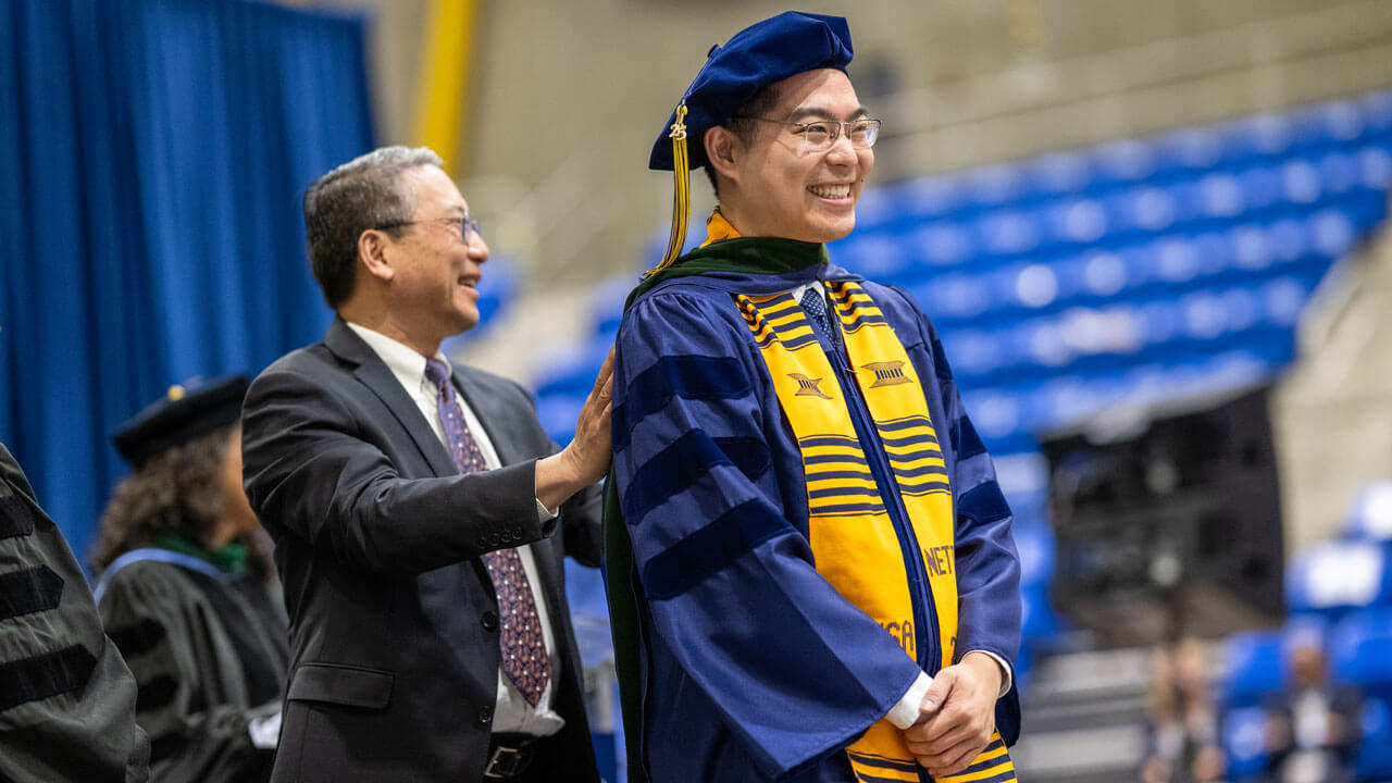 Student receives their hood on the graduation stage.