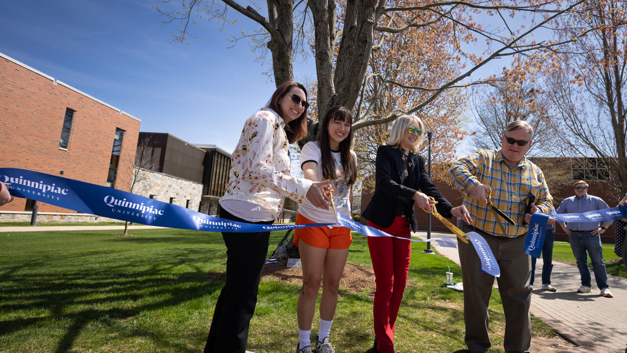 Quinnipiac employees, a student and Hamden official cut a navy Quinnipiac ribbon with large scissors