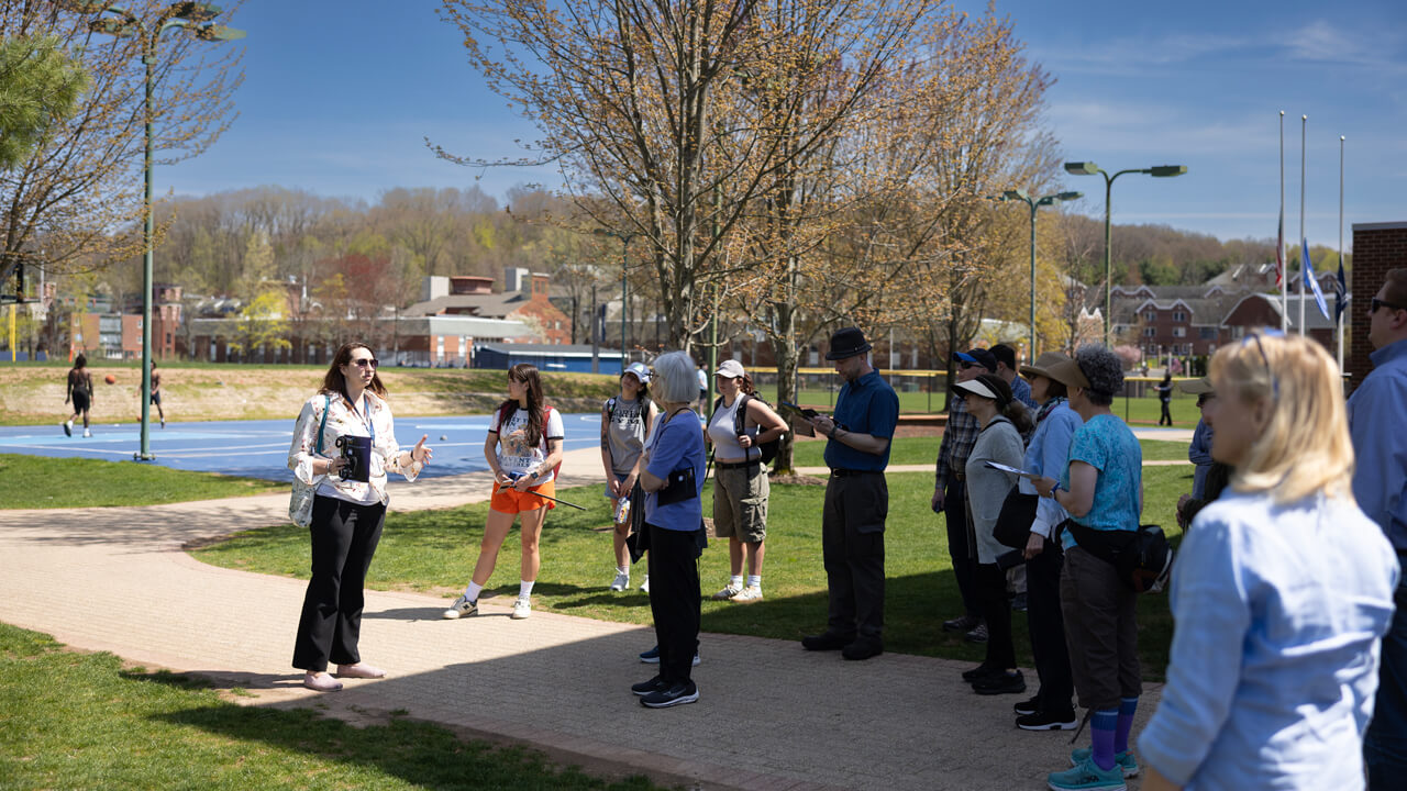 A group of participants listen to Sarah Lawson speak outside