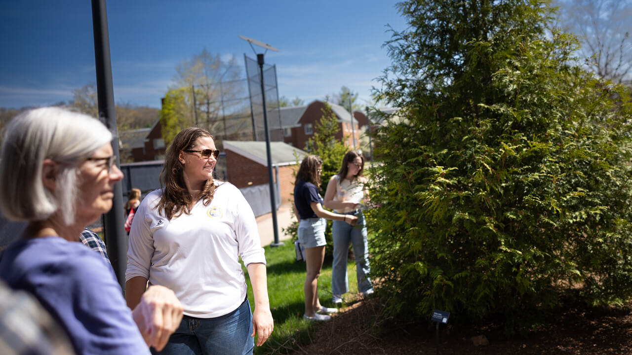 Courtney McGinnis smiles in the sun while Tree Walk participants observe trees