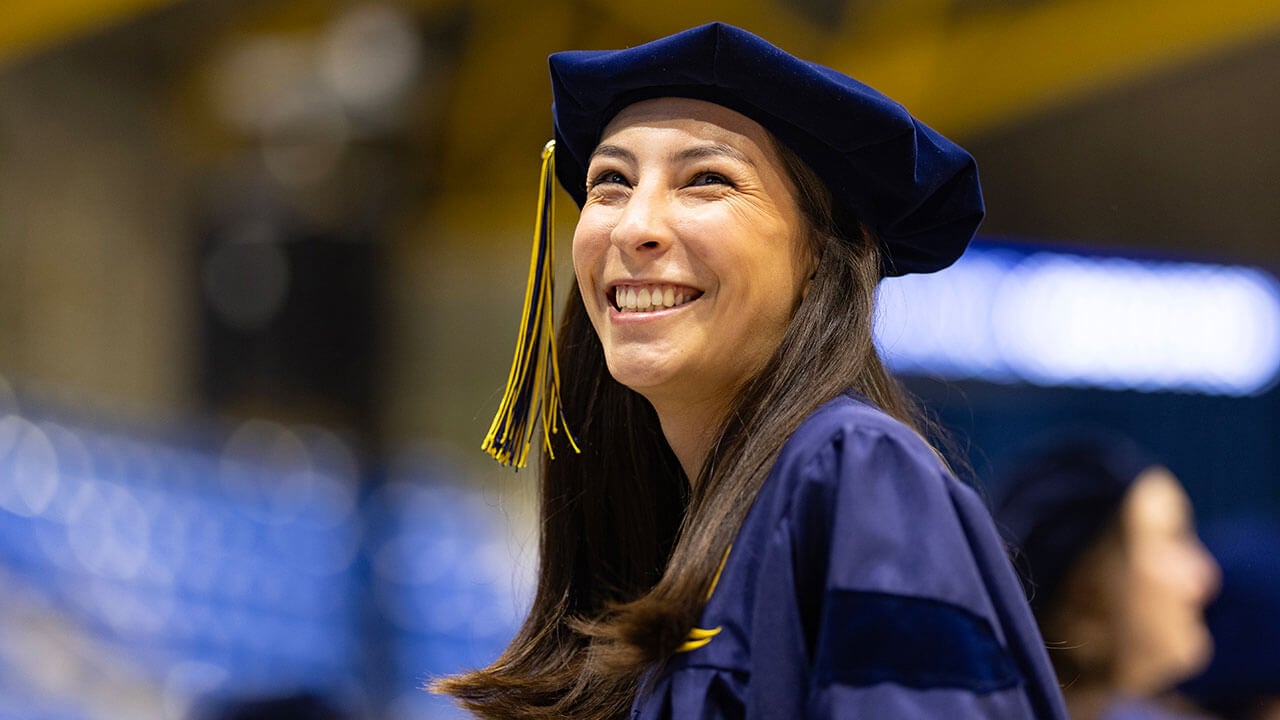 A graduate wearing a doctoral cap smiling into the distance