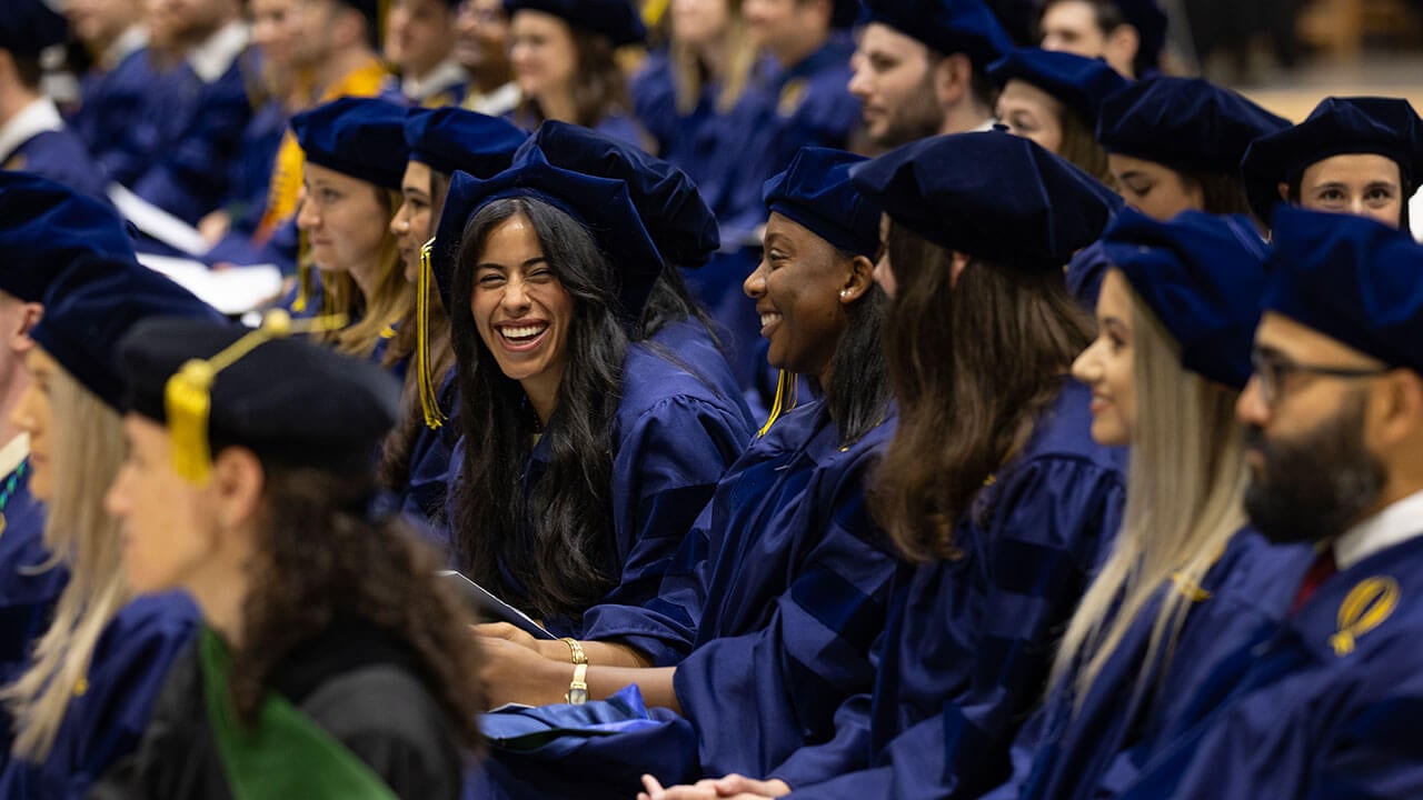 A graduate leaning over her lap and laughing