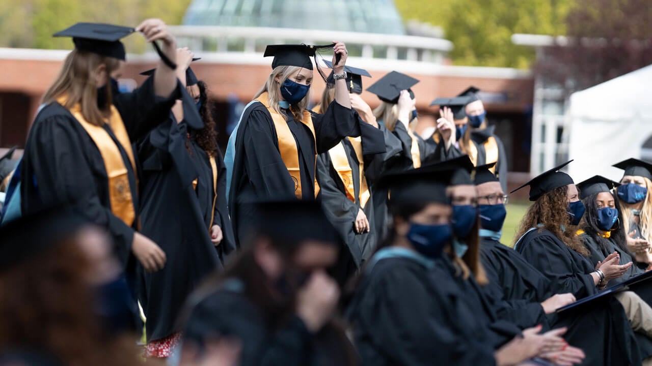 Several graduates move their tassels to the other side of their Commencement caps