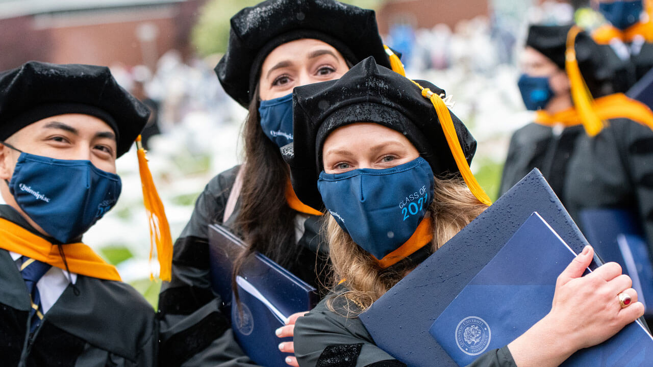 Three graduates pose with their diploma covers during Commencement