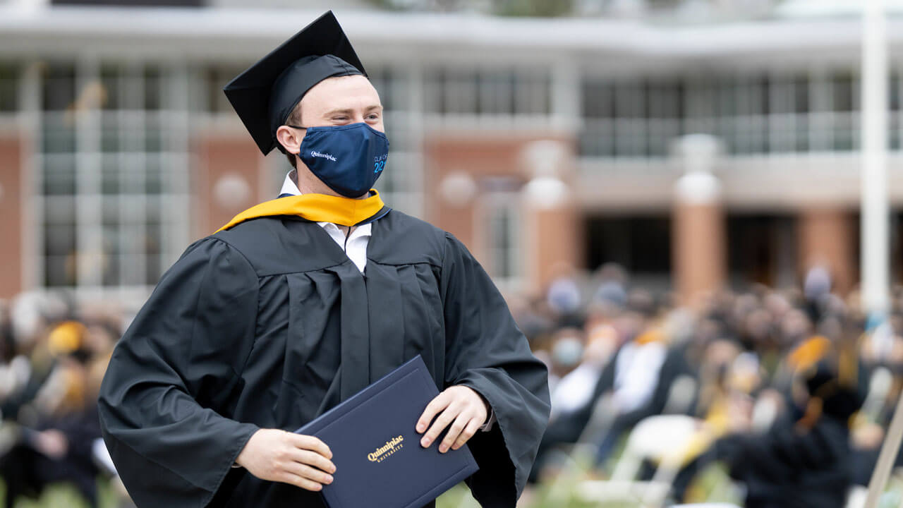 A graduate holding his diploma walks back to his seat