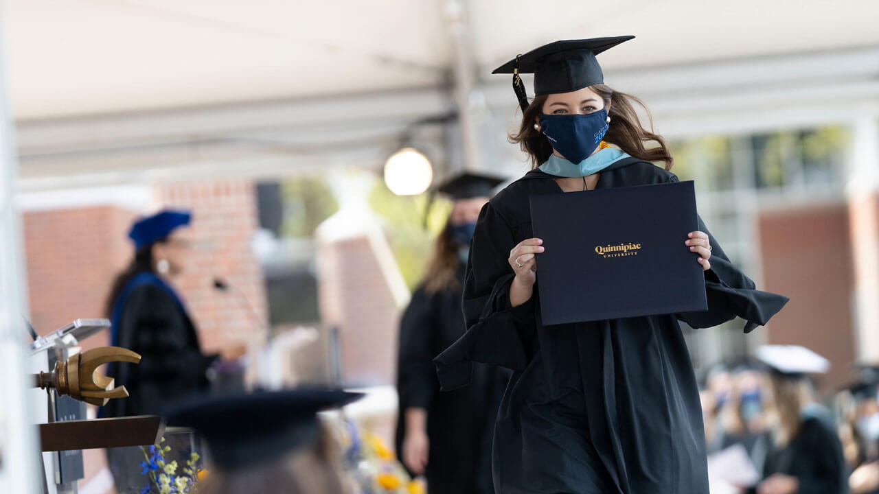 A graduate walks across the stage after receiving her diploma cover