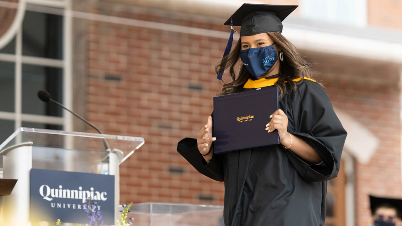 Student smiles and holds degree while walking on stage