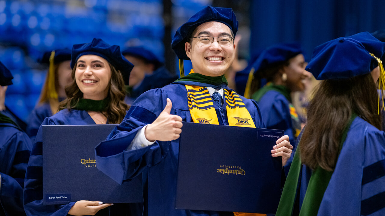 Graduate gives a thumbs up while holding their degree