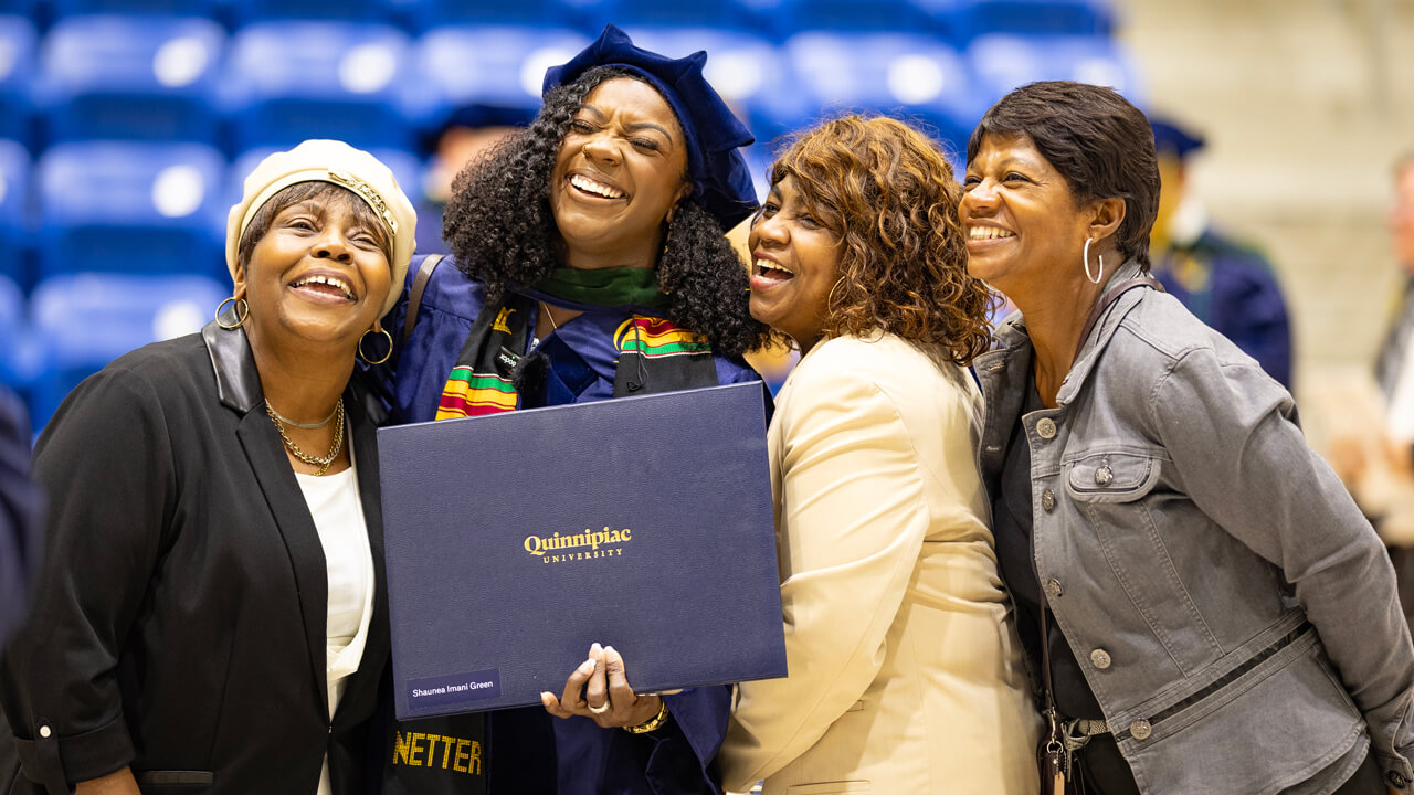 A medicine graduate smiles holding a diploma with 3 loved ones