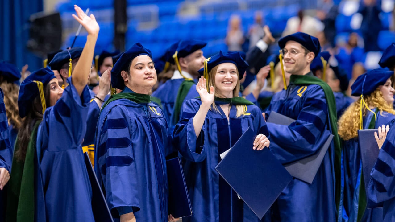 Graduates smile while holding diplomas.