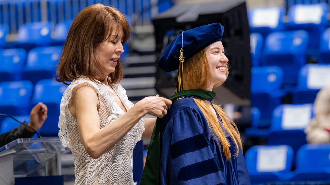 Guest assists their student as they receive their hood.