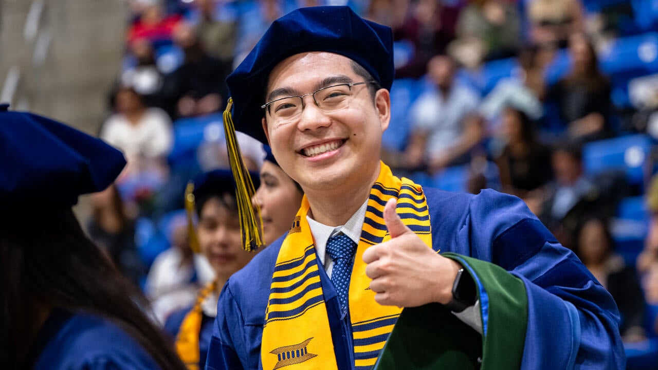 Graduate smiles with their thumb up at the camera.