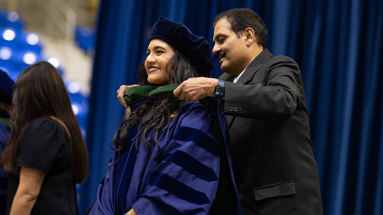 graduate receives hood from a loved one