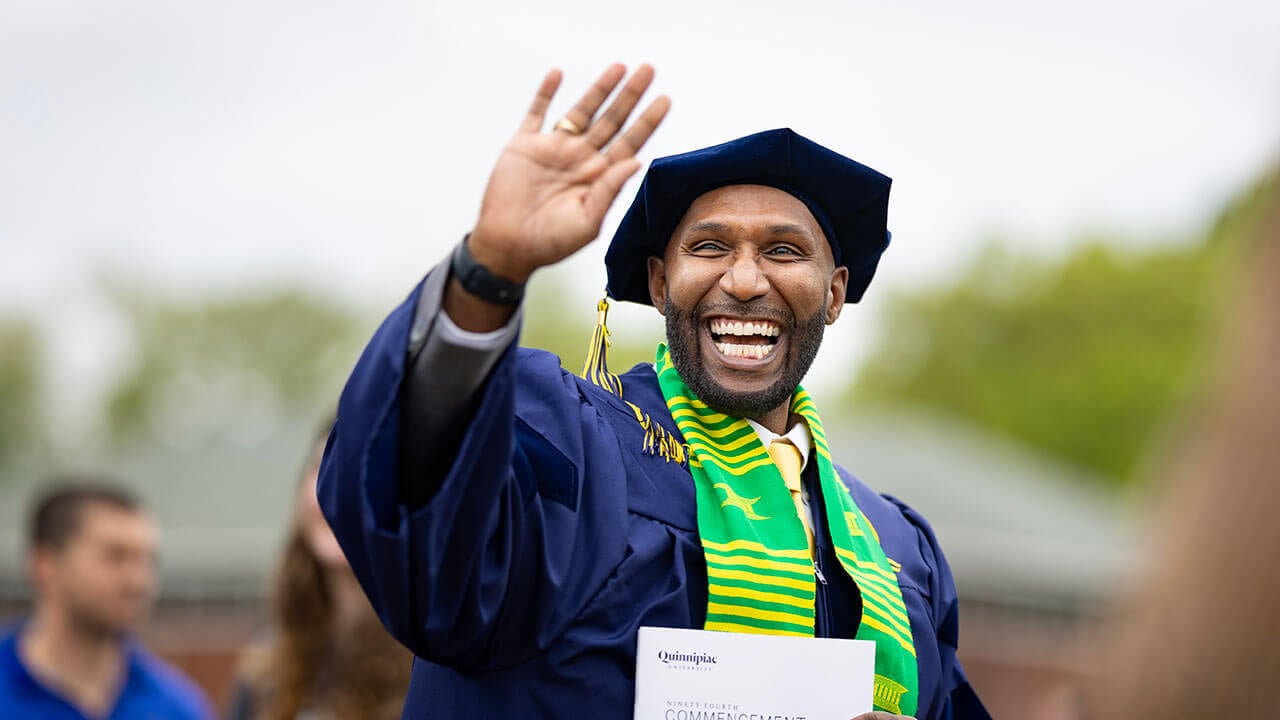 A graduate waving and smiling into the distance