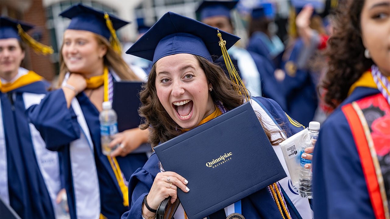 Student smiles with diploma.