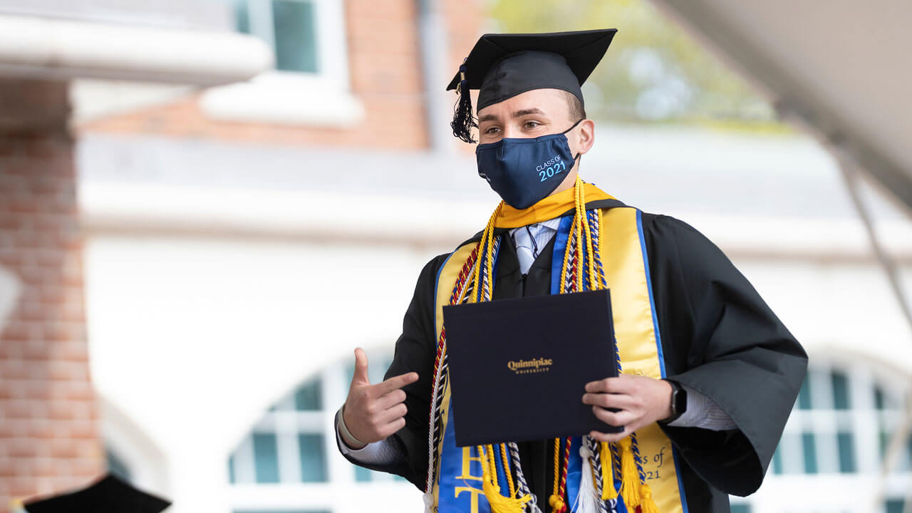 A graduate points to his diploma cover as he crosses the Commencement stage