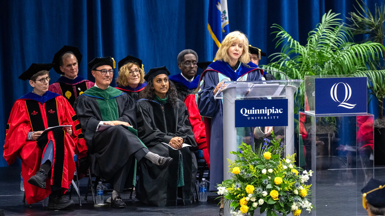 Judy Olian speaks at the podium with a number of faculty and administrators behind her