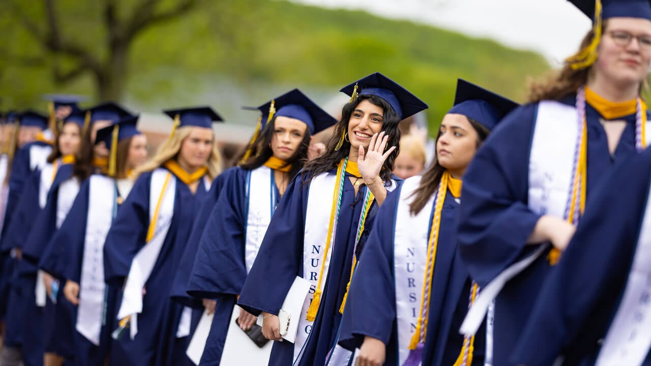 Student waves as they process into commencement.