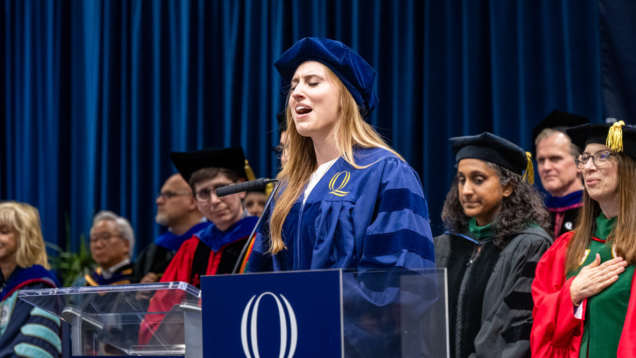 Elizabeth Landry wears her cap and gown and sings at the podium