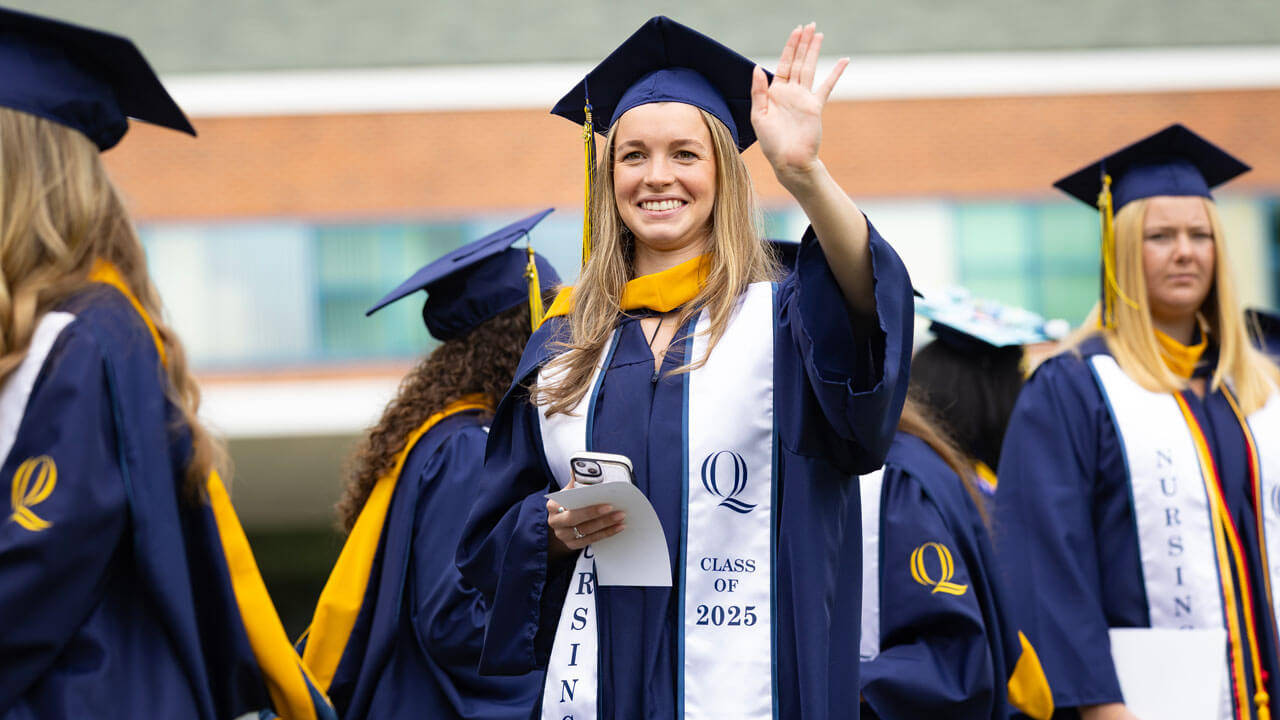 Student smiles and waves as they process into commencement.