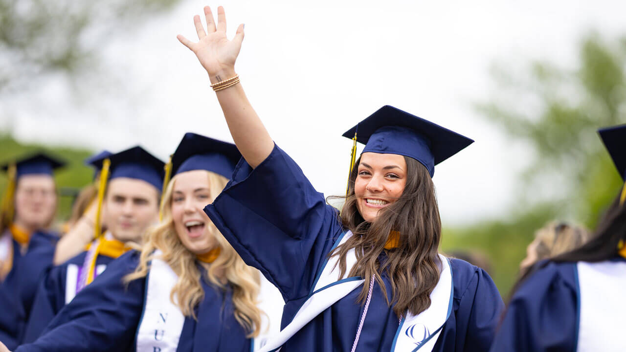 Student smiles with their arms up as they process into commencement.