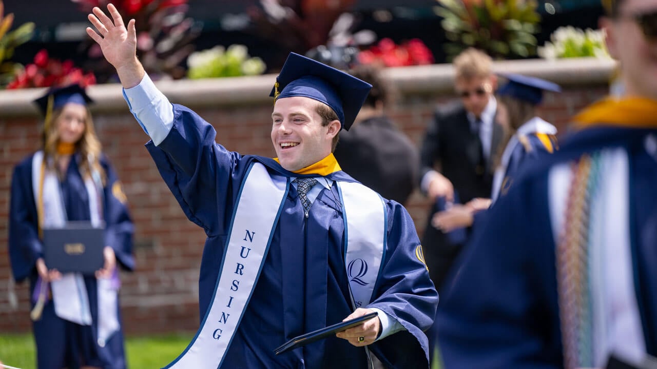 Student waves as they walk off commencement stage.