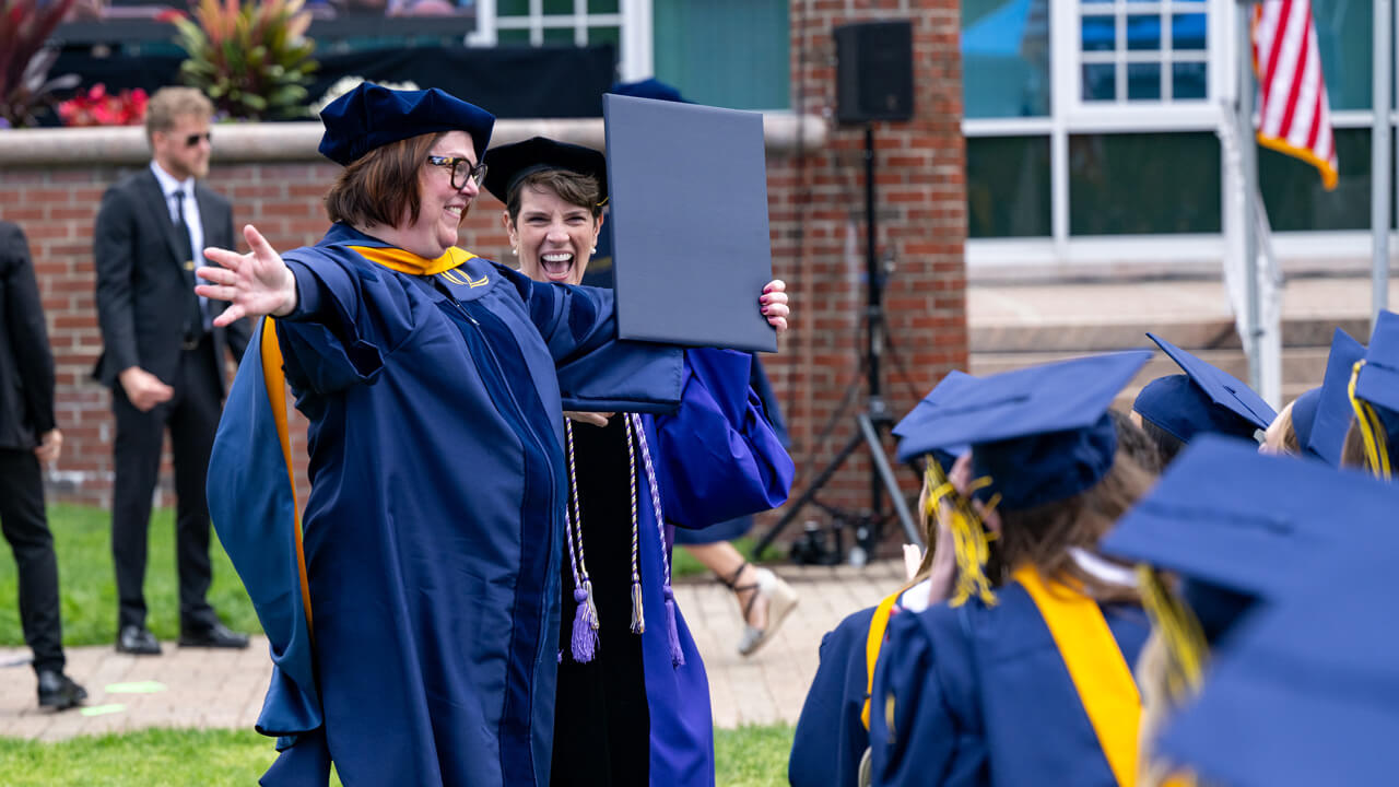 A DNP female graduate cheering holding her diploma folder
