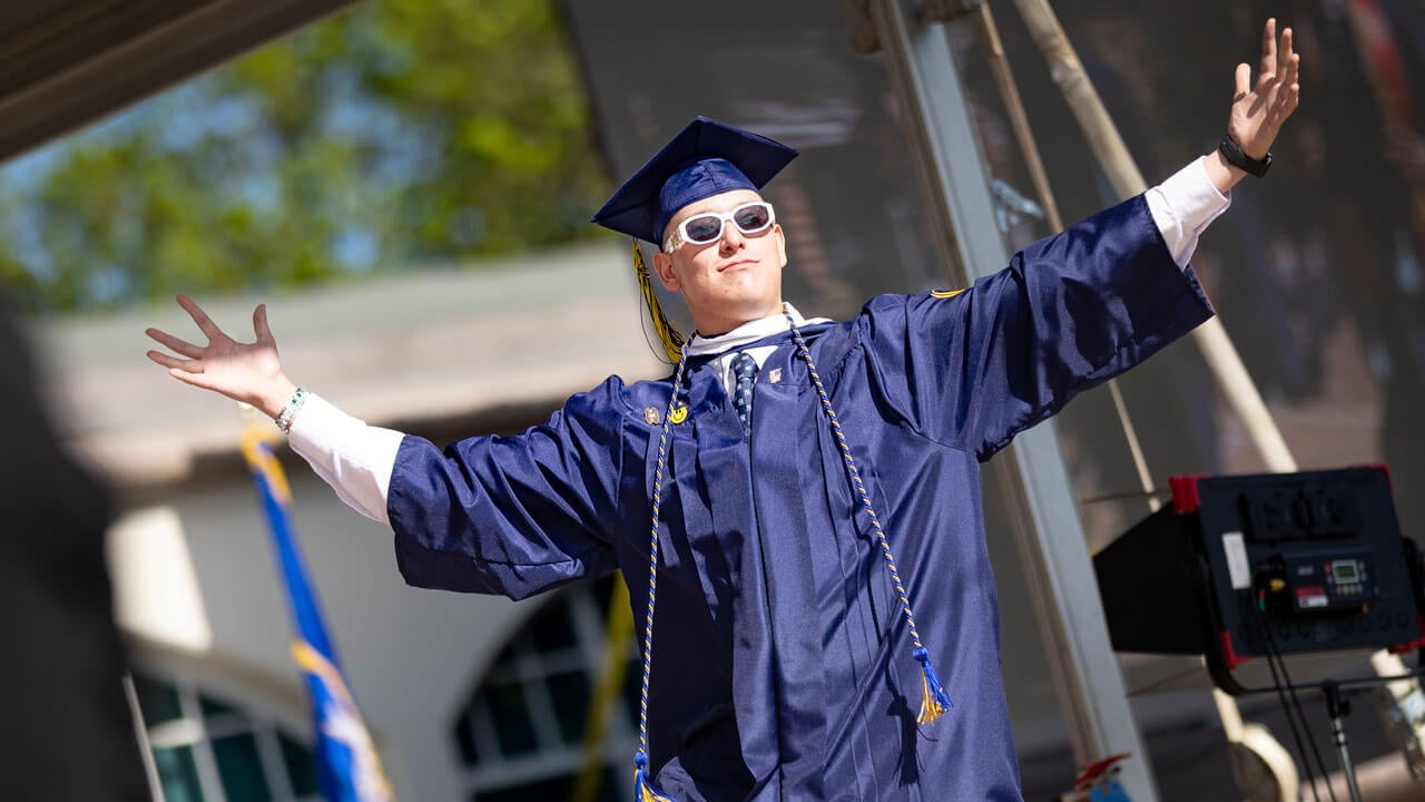 Graduate poses with their arms out as they walk across the commencement stage.