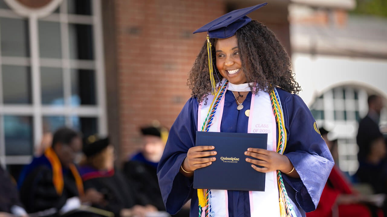 Graduate smiles as they hold their diploma.