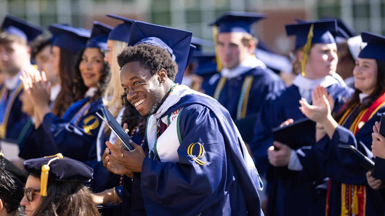 Graduate smiles and claps in the crowd.