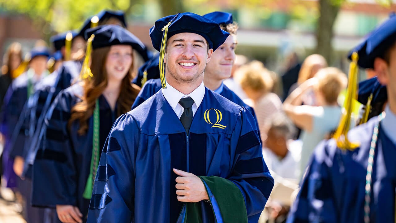 A graduate smiling and holding their hood over their arm