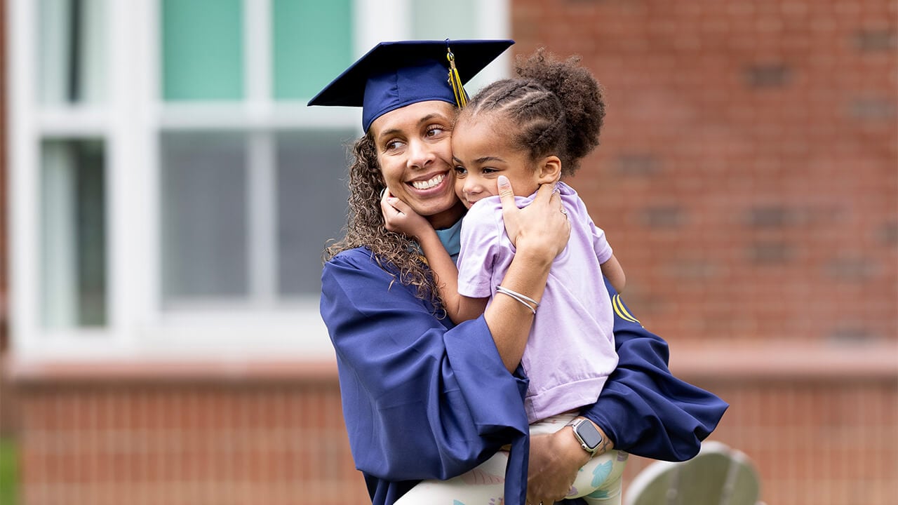 Graduating student poses with child.