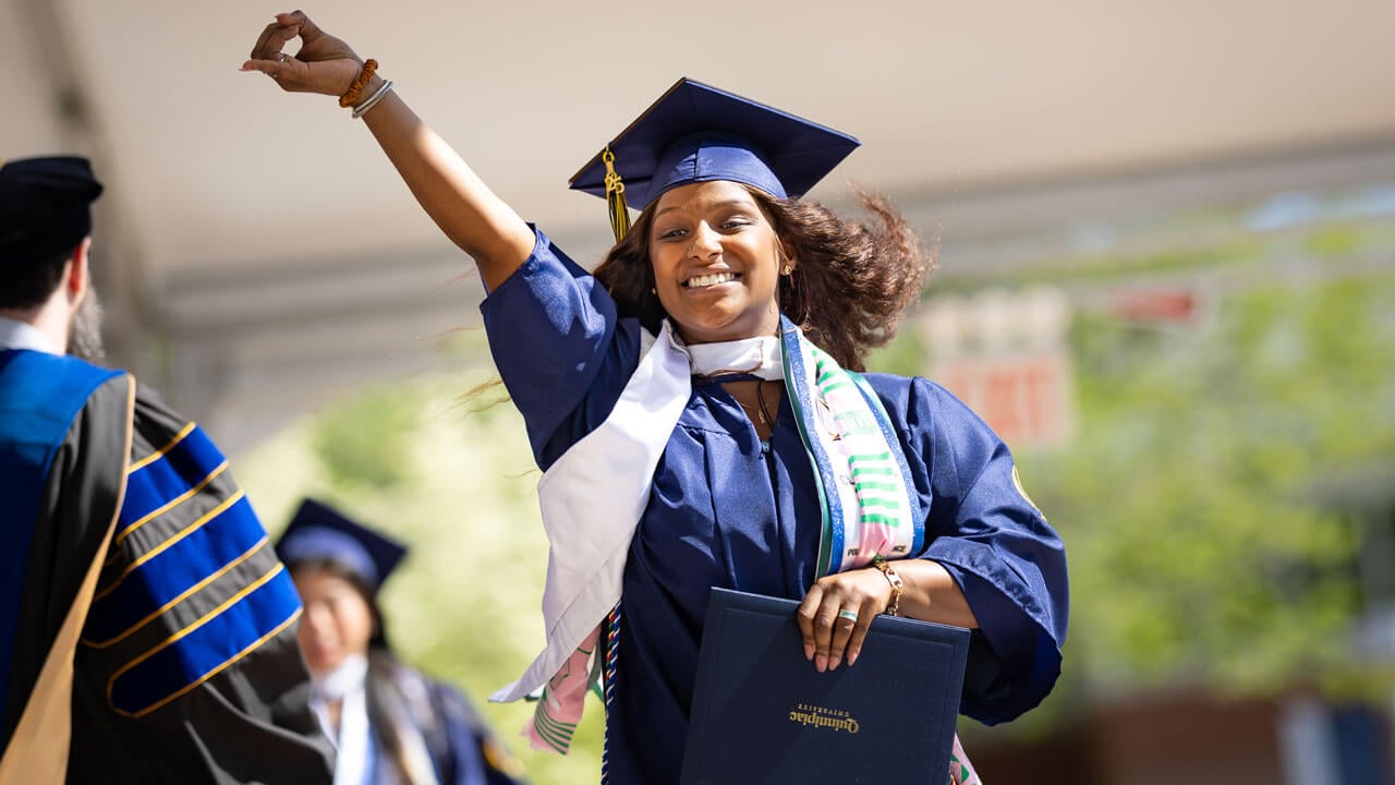 Graduate poses with their hand up as they accept their diploma.