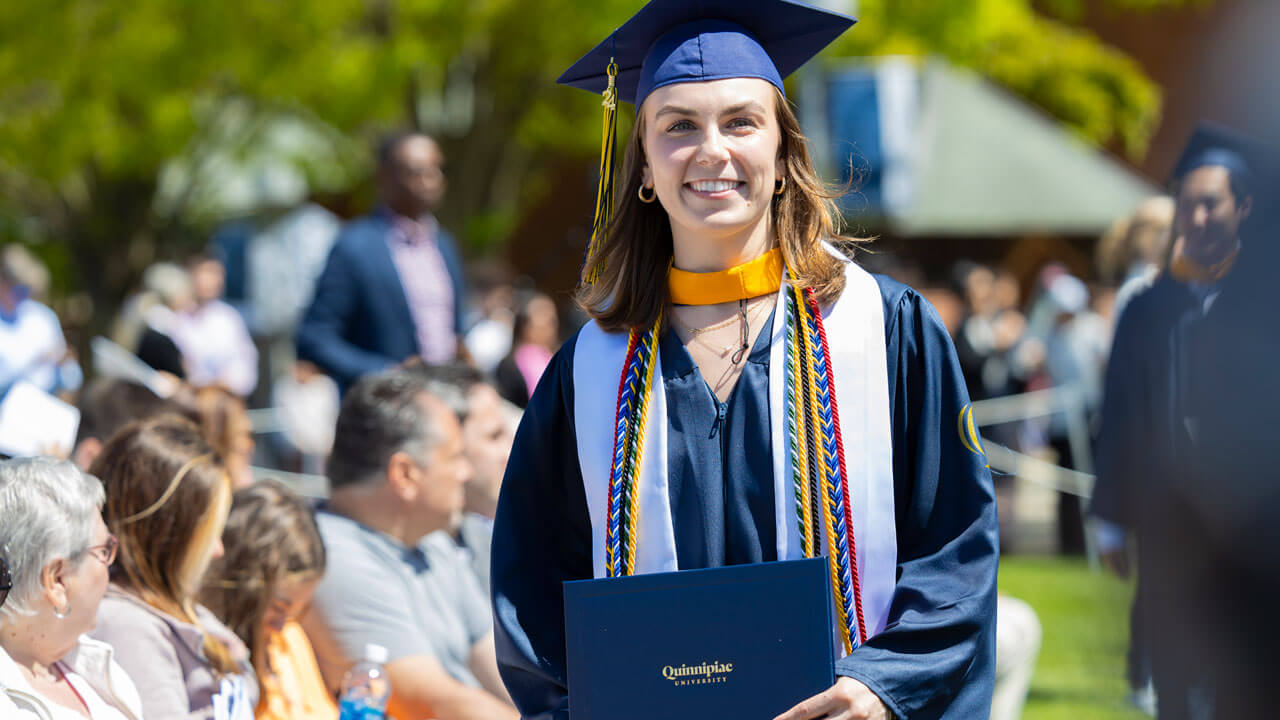 Decked out in academic regalia, a graduate of the School of Business class of 2024 grins ear to ear after receiving their diploma..