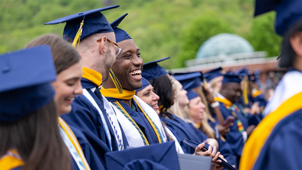 Students in caps and gowns laugh at commencement.