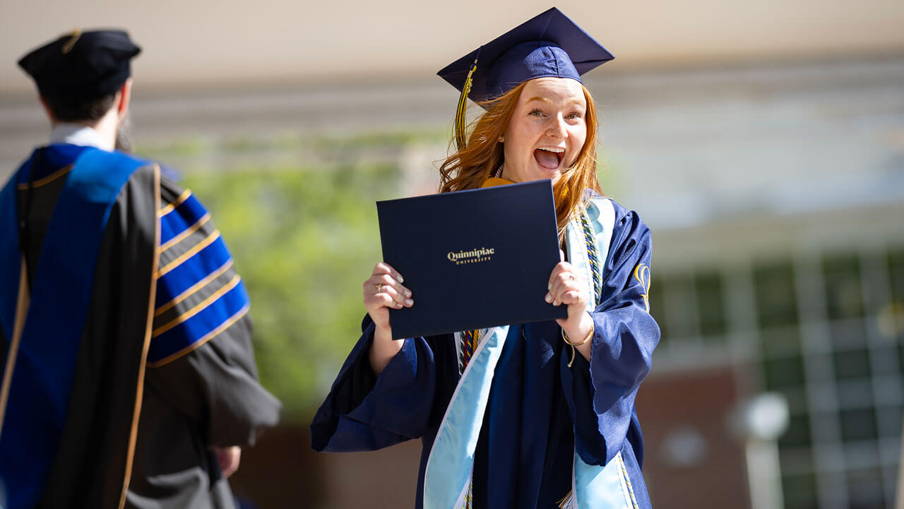 Graduate smiles in excitement with their diploma as they exit the commencement stage.