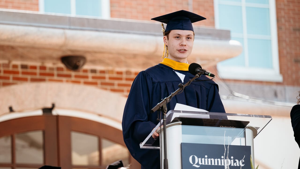 Anton Petrenko wears Commencement gown and cap and speaks at a podium