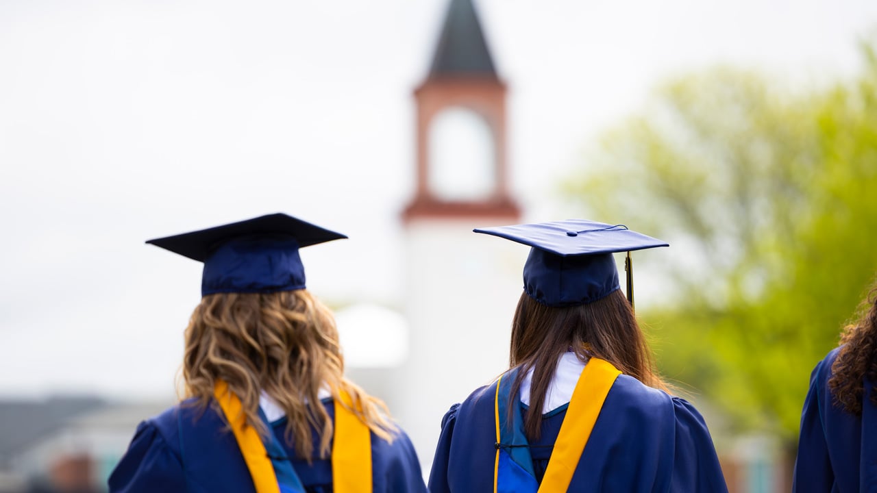 Back of 2 girls in cap and gowns with clocktower in the blurry background