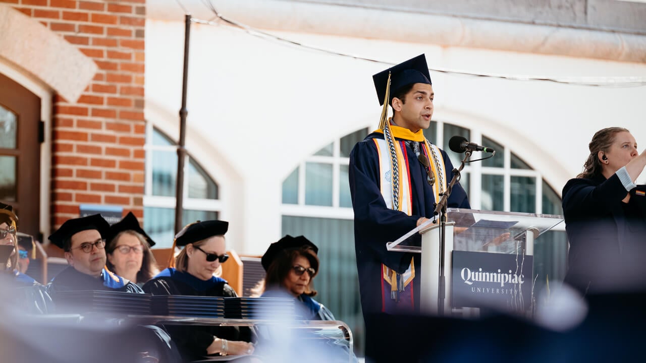 Moinuddin Mohmed Faruk Kothawala speaks at a podium in this Commencement robe and cap