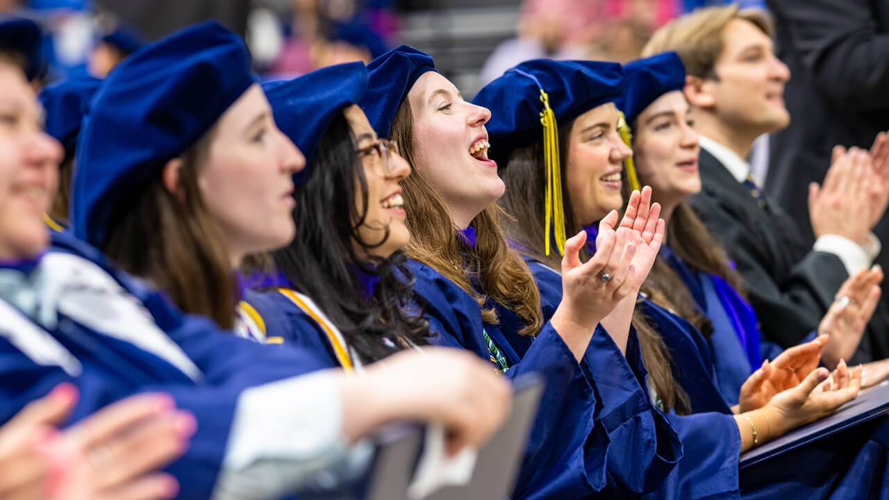 A row of graduates clap and smile from their seats