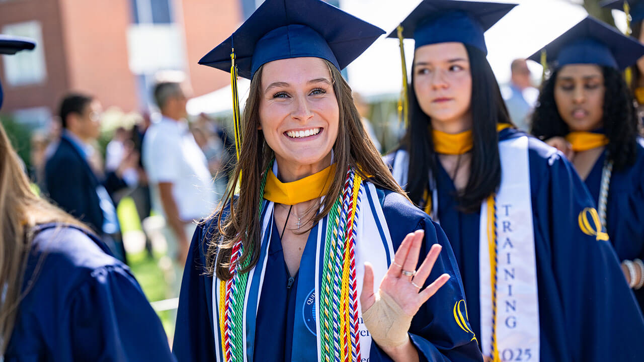 A graduate smiling and waving into the distance
