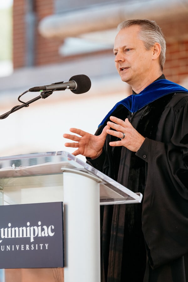 Richard Benton holds up his hands as he speaks at a podium during Quinnipiac Commencement