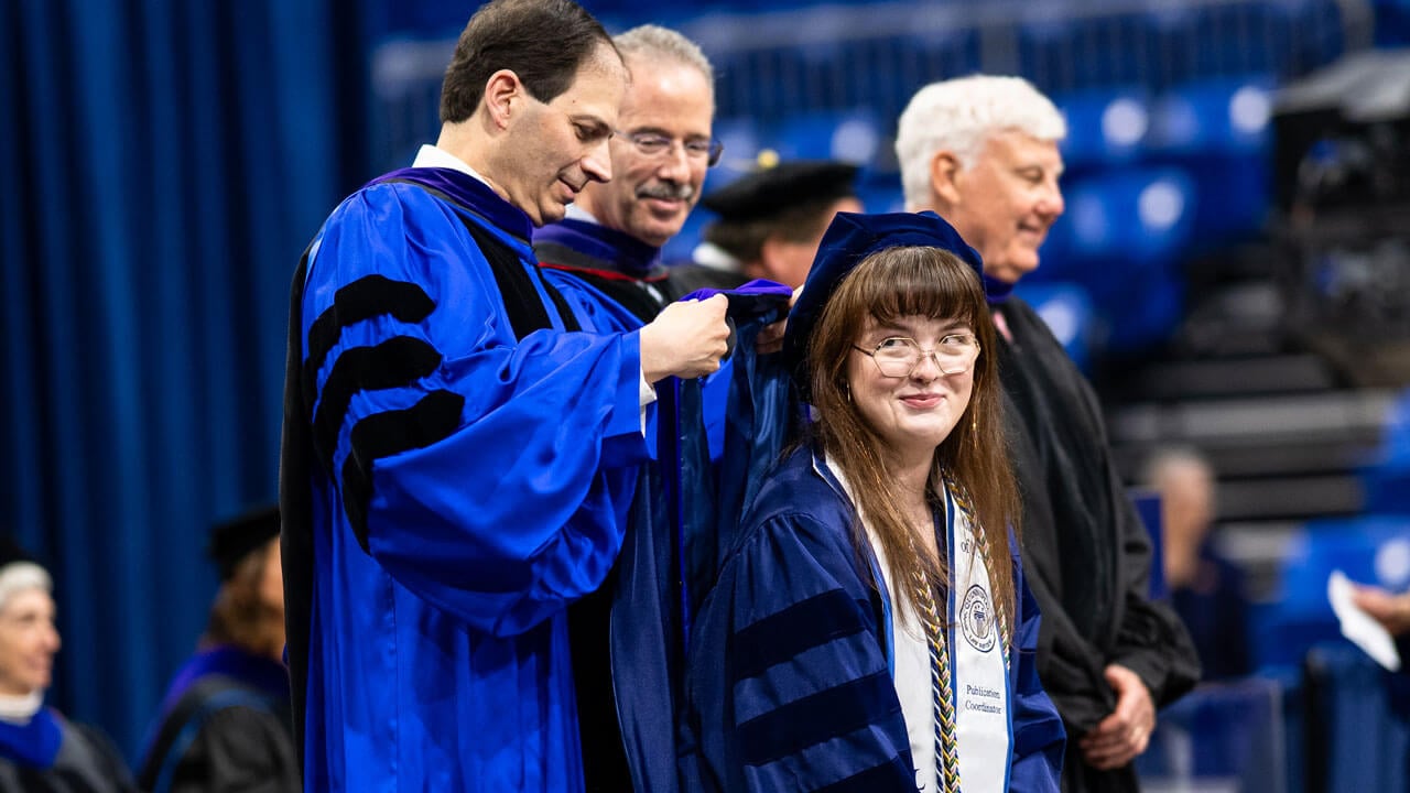 Faculty member places hood over graduate.
