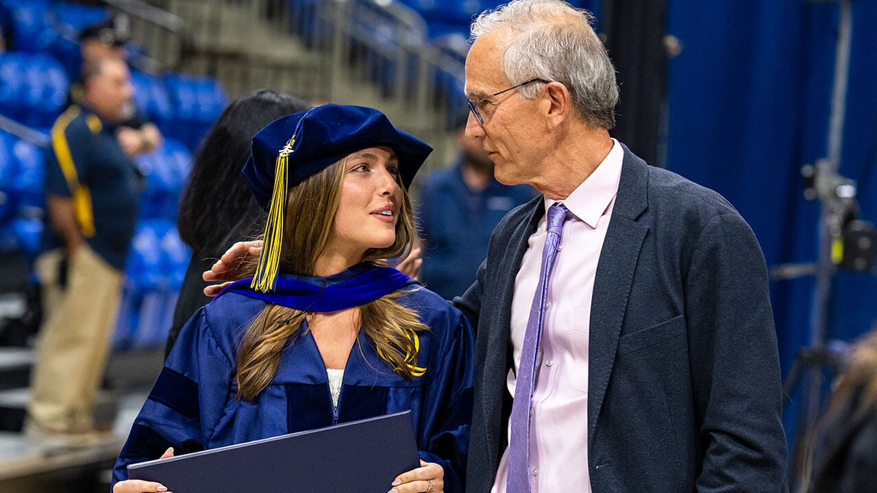 A graduate walking off stage with a family member and smiling at one another