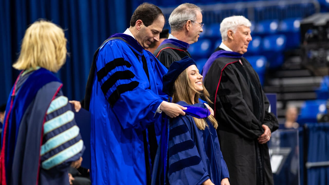 Faculty member places hood over graduate.
