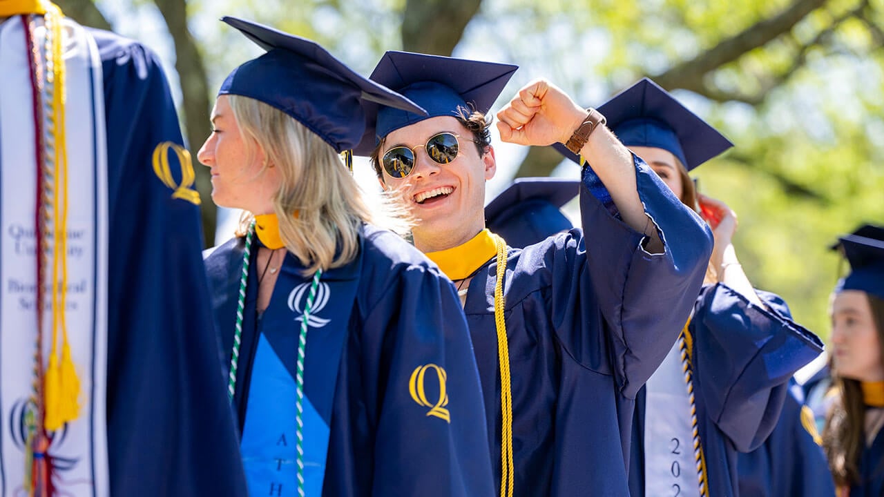 Grad in cap and gown pumps his arm in the air while walking in a procession