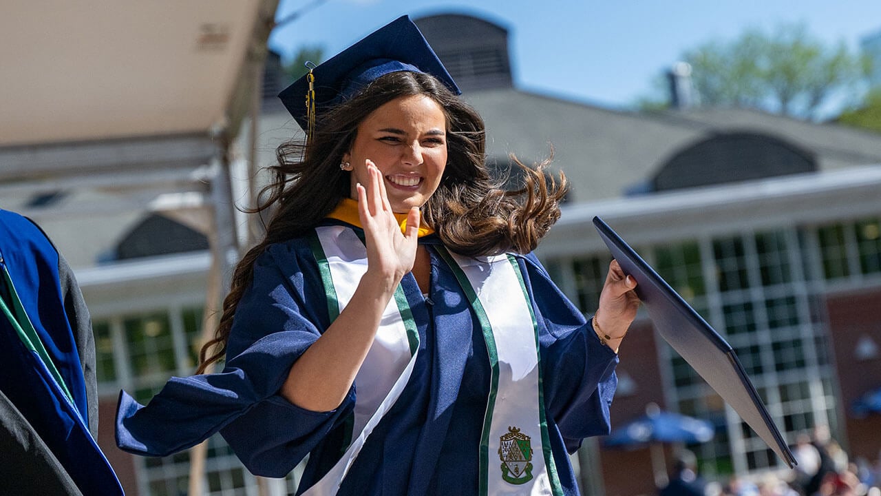 graduate waves at the livestream camera with diploma