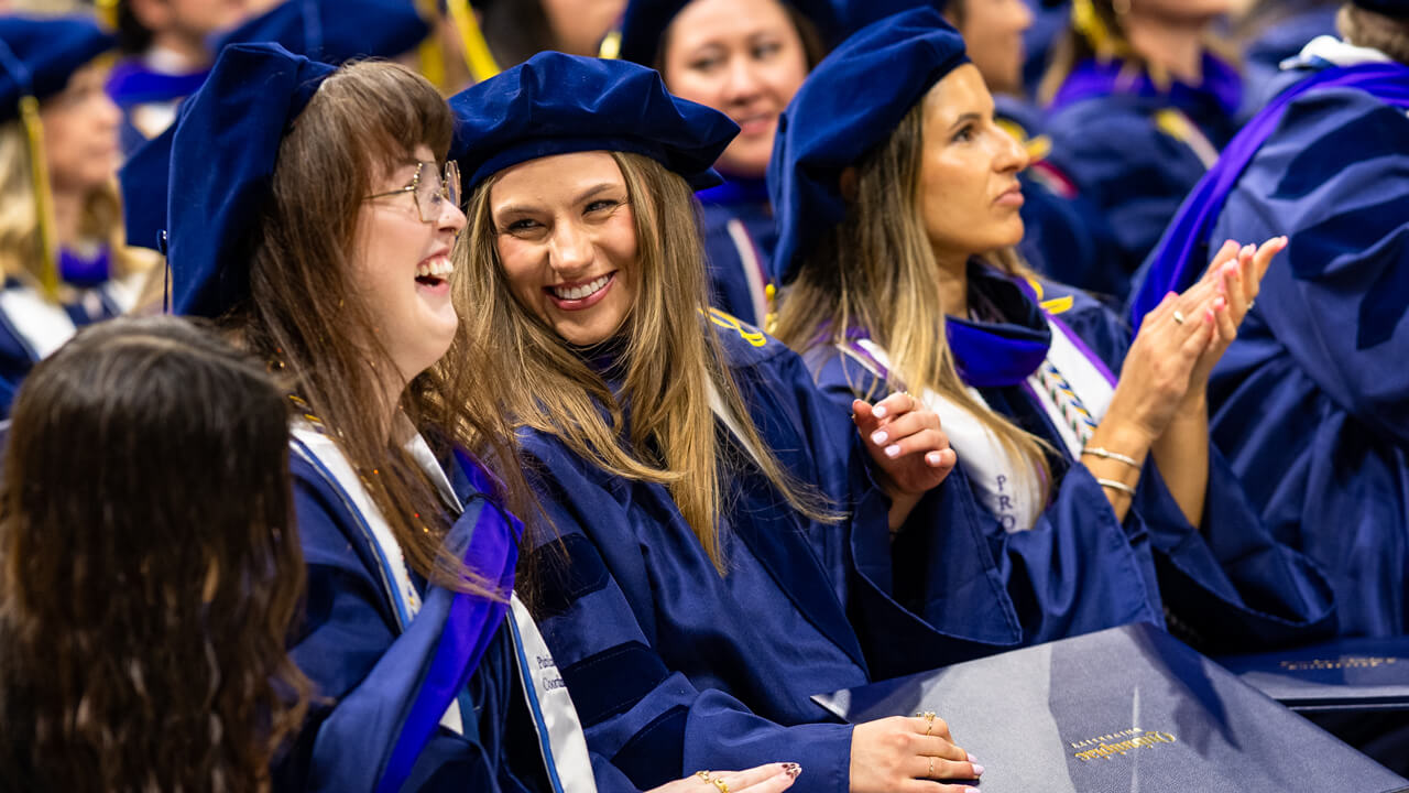 Two graduates seated together smile with each other during the Commencement ceremony