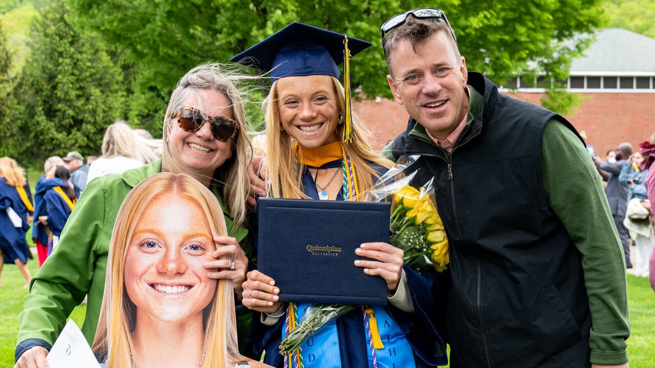 Graduate poses with their loved ones as they hold a cut-out of their student.