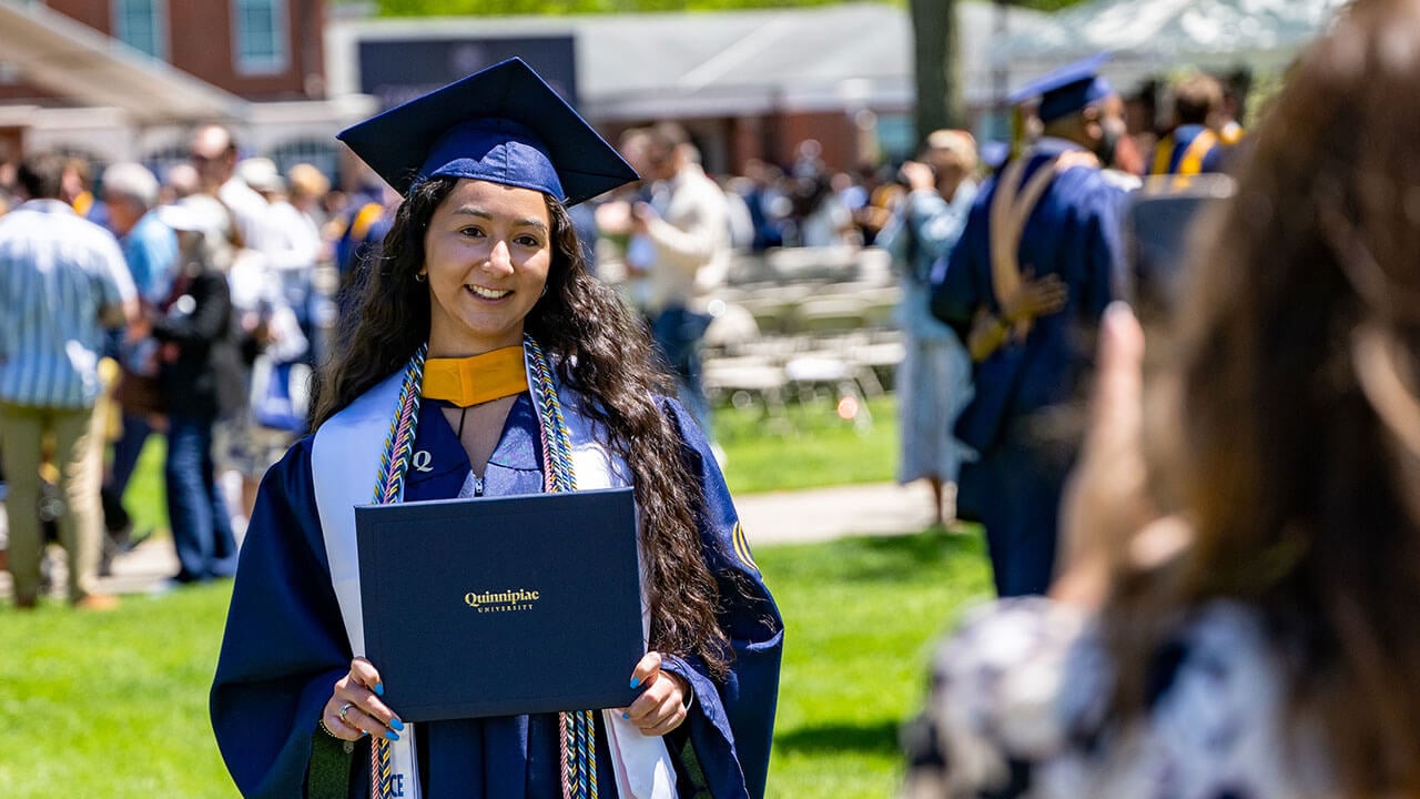 A graduate holding their diploma and smiling